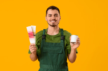 Young painter with can of paint and color palettes on yellow background