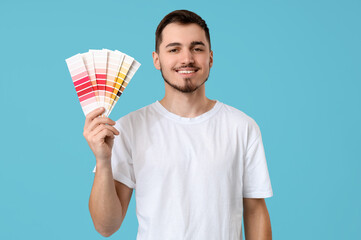 Young man with paint palettes on blue background