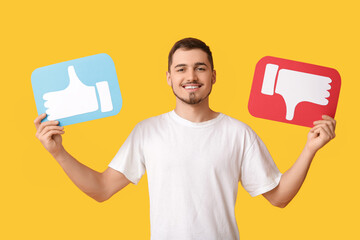 Handsome young happy man with like and dislike icons on yellow background