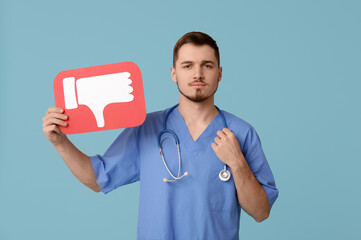 Handsome young male doctor with dislike icon on blue background
