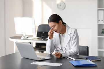 Tired young Asian businesswoman with eyeglasses working at table in office