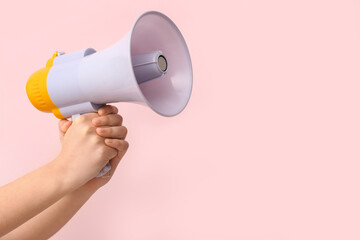 Female hands with megaphone on pink background