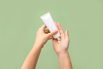 Woman applying cosmetic cream on green background