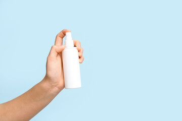 Female hand with bottle of cosmetic spray on blue background