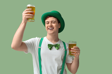 Happy young man in leprechaun's hat with glasses of beer on green background. St. Patrick's Day...
