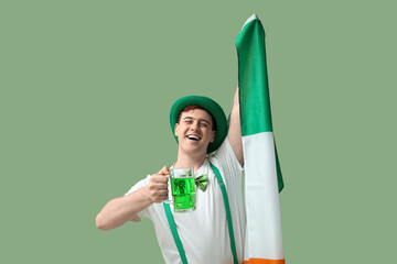 Happy young man in leprechaun's hat with beer and flag of Ireland on green background. St....