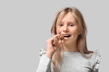 Cute little girl with sweet chocolate candy on grey background