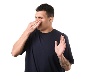 Handsome young man pinching nose because of bad smell on white background