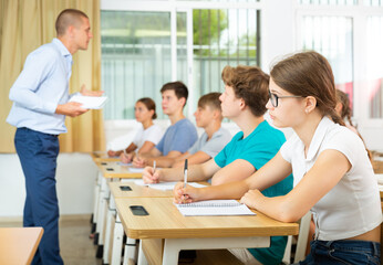 Obraz premium Teenage students studying in classroom with teacher, writing lectures in workbooks