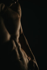 Close-up of a muscular male torso in low light, highlighting defined abs and strong physique, representing fitness, strength, and healthy lifestyle