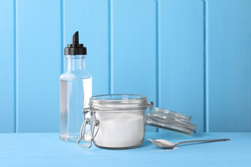 Natural cleaning products. Vinegar in bottle, baking soda and spoon on light blue wooden table