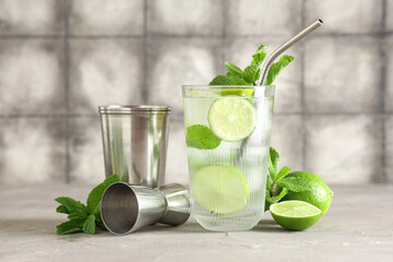 Glass of fresh Mojito cocktail with limes and mint on grey table