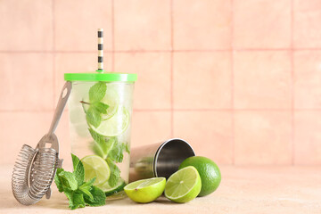 Glass of fresh Mojito cocktail with limes and mint on beige table