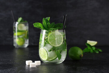 Glass of fresh Mojito cocktail with limes and mint on black background