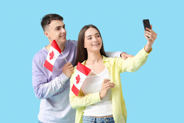 Young couple with flags of Canada taking selfie on blue background