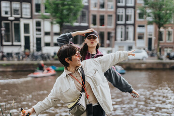 Two friends enjoying their time by a canal in Amsterdam, having fun and striking playful poses. The...