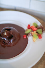 Pouring chocolate sauce over chocolate dome decorated with strawberry and kiwi in white plate. Delicious fresh dessert.