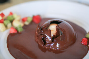 Pouring chocolate sauce over chocolate dome decorated with strawberry and kiwi in white plate. Delicious fresh dessert.