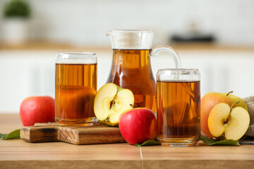Glasses and jug of fresh apple juice on wooden table in kitchen