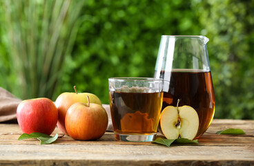 Glass and jug of fresh apple juice on wooden table outdoors