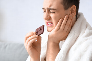 Young man with chocolate suffering from toothache in living room