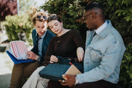 Three diverse business colleagues engage in a focused outdoor meeting in the city, reviewing and discussing statistical data and documents.