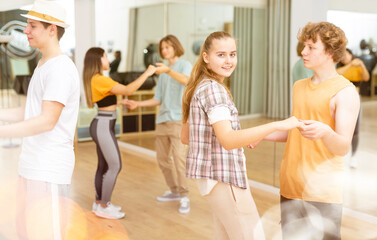 Pairs of teengers standing in dance studio and holding each other hands during their repetition.