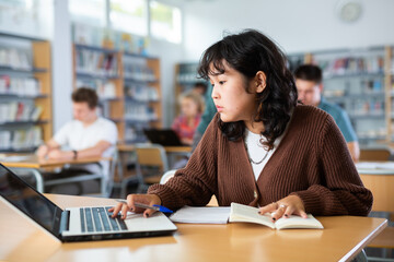Portrait of diligent asian college girl studying in library using laptop