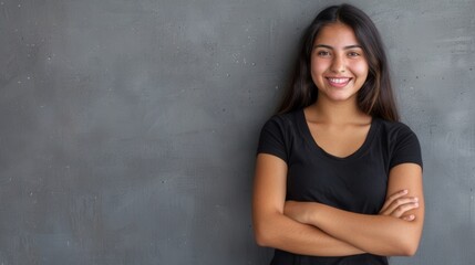 Fototapeta premium A young Hispanic woman with long, dark hair stands against a grey wall, smiling cheerfully with her arms crossed. Generative AI