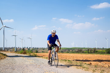 Naklejka premium Caucasian active sportsman riding bicycle at the wind turbine field. 