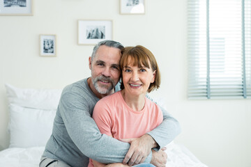 Portrait of Caucasian senior elderly couple sitting on bed in bedroom. 