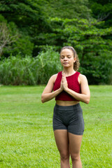 Young healthy hispanic woman using sportwear doing yoga in a public park. Mindful and meditation concept. Namaste. Prayer pose. Pranamasana