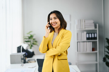 Confident Asian Business Woman in Yellow Blazer Talking on Phone in Modern Office Setting