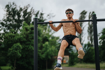 Obraz premium Athletic man performing pull-ups on metal bars in an outdoor park, showcasing strength and fitness.