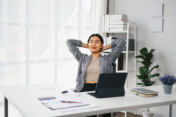 Naklejka premium Confident Asian Business Woman Relaxing at Modern Office Desk with Laptop and Documents