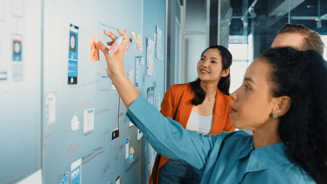 Portrait Of Group Of Businesspeople Putting Sticky Notes On Glass Board. Professional Business Team Brainstorming Marketing Strategy While Stick Notes On Glass Wall. Business Meeting. Manipulator.