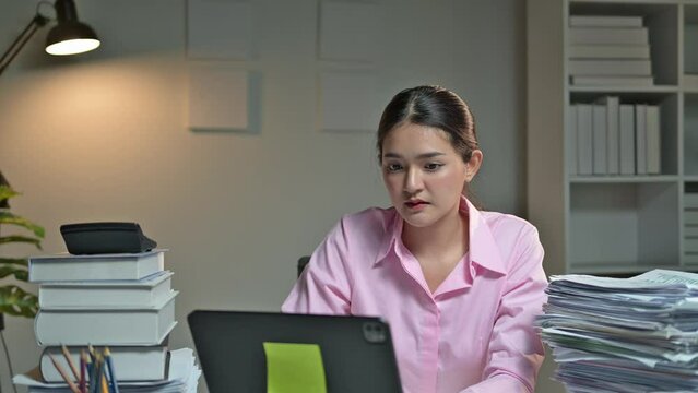 Stressed office worker in modern office overwhelmed at desk with laptop and paperwork, burying face in hands. Job pressure, fatigue, and emotional stress in corporate environment