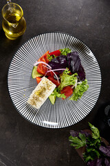 Fresh Greek Salad with Feta Cheese Garnished with Herbs on Black Striped Plate