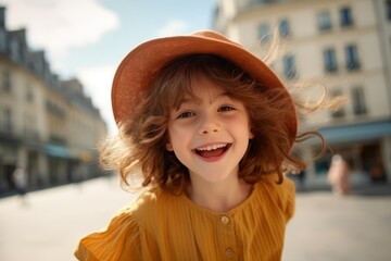 Portrait of smiling little girl in hat looking at camera on street