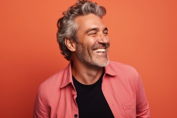 Obraz premium Portrait of a handsome middle-aged man laughing and looking at the camera while standing against orange background