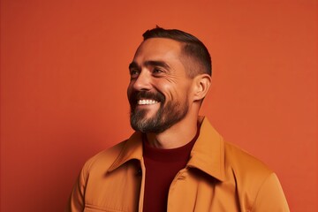 Obraz premium Portrait of a smiling bearded man in a brown jacket on a red background.