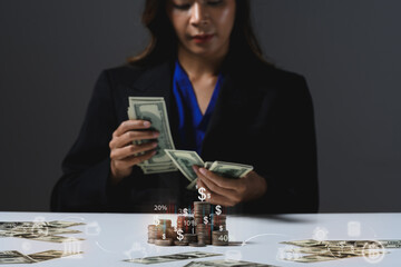 Businesswoman counting dollar bills at desk with scattered dollar bills and coin stacks . Wealth, investment and financial growth