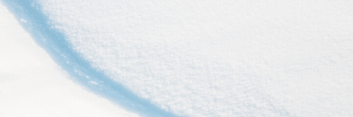 Wide panoramic winter background with snowy ground. Natural snow texture. Wind sculpted patterns on snow surface. Closeup top view with copy space.