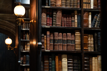 Fototapeta premium JAPAN - Nov 13, 2023: Hogwarts library with vintage bookshelves filled with old leather bound books illuminated by antique wall lamps at Warner Bros. Studio Tour Tokyo, The Making of Harry Potter