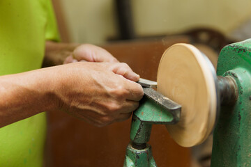 A man is working on a carpentry project, using an antique green wood polishing tool that he rotates to shape a round piece of wood.