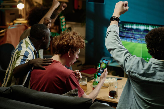 Group of multi-ethnic cheerful soccer fans enjoying watching match livestream on TV late in evening