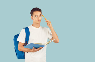 Portrait of thinking brunette boy holding pen and textbook in hands with backpack on back isolated...