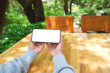 Mockup image of a woman holding mobile phone with blank white desktop screen in the outdoors