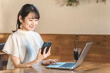 カフェや喫茶店でパソコンを使ってテレワーク・仕事をするアジア人のビジネスウーマン
