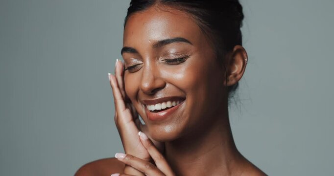 Skincare, face and beauty of happy Indian woman in studio isolated on gray background. Touch, smile and young model in makeup for facial cosmetics, dermatology or healthy glow with eyes closed at spa